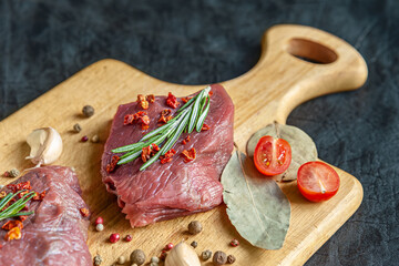 raw meat with spices, cherry tomatoes and garlic on a wooden cutting board close up