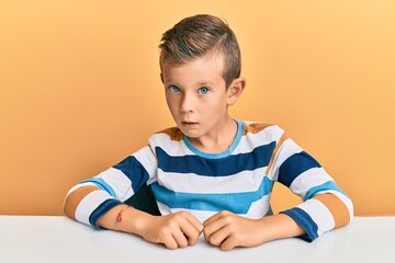 Adorable caucasian kid wearing casual clothes sitting on the table in shock face, looking skeptical and sarcastic, surprised with open mouth