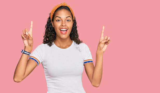 Young african american girl wearing casual clothes smiling amazed and surprised and pointing up with fingers and raised arms.