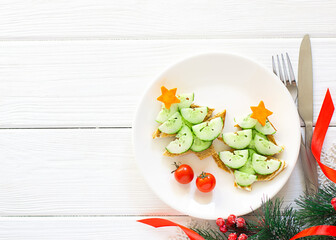 Creative idea for decorating New Year's snacks. Vegetarian and dietary concept. Sandwiches in the form of a Christmas tree with a cucumber and a carrot,tomatoes on a plate on a white wooden background