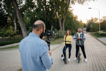 They shoot a video blog about a young beautiful couple riding electric scooters in a Park on a warm autumn day. Hobbies and recreation.