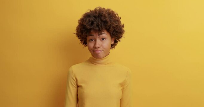 Puzzled unaware woman shrugs shoulders and lookd doubtful at camera being uncertain doesnt know what to answer isolated over yellow background. People perception and human expressions concept