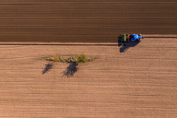 Luftaufnahme eines Traktors beim Umpflügen eines Ackers neben einem kleinen Blühstreifen für Biodiversität © reisezielinfo