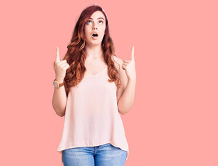 Young beautiful woman wearing casual clothes and diadem amazed and surprised looking up and...