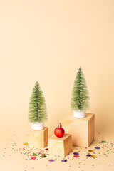 New year creative concept. Two artificial Christmas trees, red Christmas decoration on wooden cubes and multicolored confetti around on a beige background. Christmas background.Minimalism