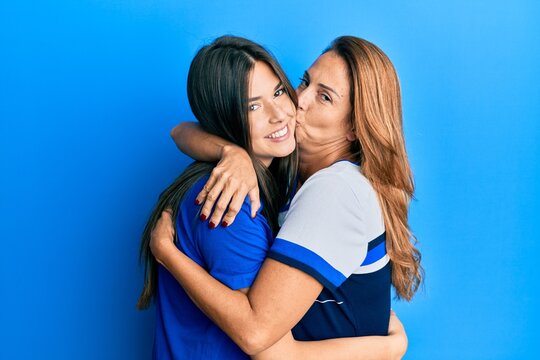 Beautiful hispanic mother and daughter smiling happy hugging and kissing over isolated blue background.