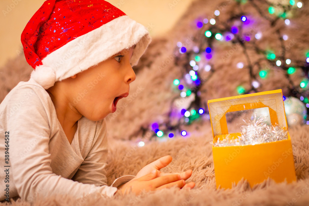 Wall mural child in santa claus hat surprised at gifts