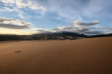 Smooth Sand Dunes and Mountains Enveloped in Clouds