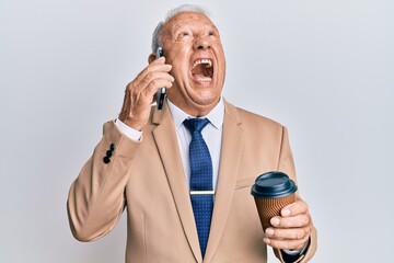 Naklejka premium Senior caucasian man talking on the smartphone and drinking a cup of coffee angry and mad screaming frustrated and furious, shouting with anger looking up.