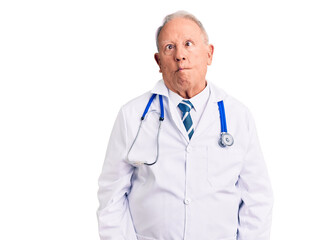 Fototapeta premium Senior handsome grey-haired man wearing doctor coat and stethoscope making fish face with lips, crazy and comical gesture. funny expression.