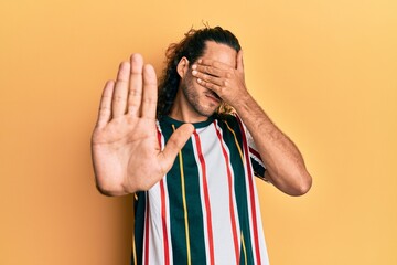 Young handsome man with long hair wearing casual clothes covering eyes with hands and doing stop gesture with sad and fear expression. embarrassed and negative concept.