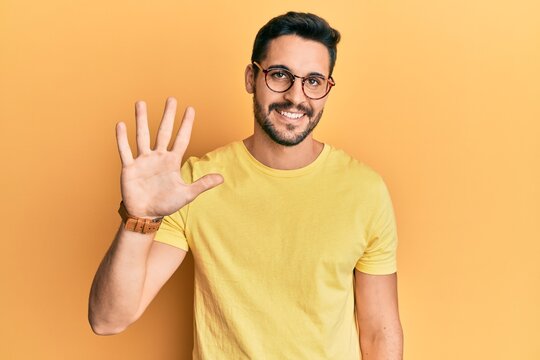 Young hispanic man wearing casual clothes and glasses showing and pointing up with fingers number five while smiling confident and happy.