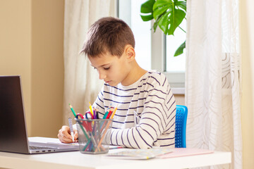 School pupil with laptop computer writing notebook doing homework at table. Online learning, remote education, distance lessons at home