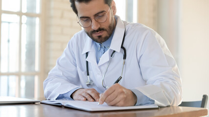 Serious attentive young male doctor qualified specialist surgeon therapist focused on filling...