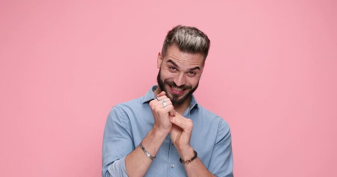 casual attractive man rubbing his palms and hiding a diabolically plan against pink background