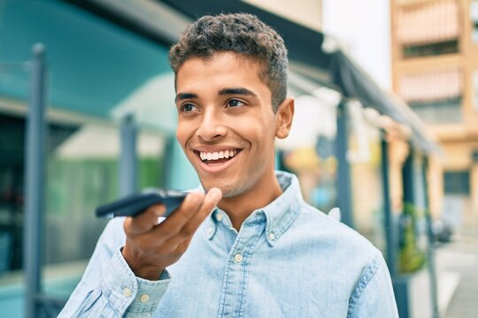 Young latin man smiling happy sending voice message using smartphone at the city.