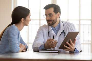 Look at screen, please. Positive capable doc general practitioner demonstrating test results in electronic format or illustrating illness concept to curious patient holding digital tablet pc in hands