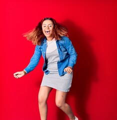 Young beautiful latin woman wearing casual clothes smiling happy. Jumping with smile on face doing winner gesture with fists up over isolated red background