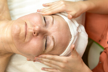 Cosmetologist doing massage for senior woman at spa salon. Anti-aging facial massage concept.