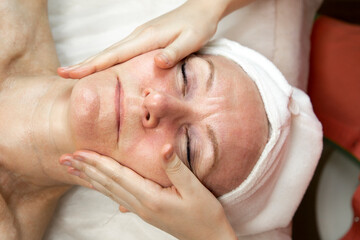 Fototapeta na wymiar Cosmetologist doing massage for senior woman at spa salon. Anti-aging facial massage concept.