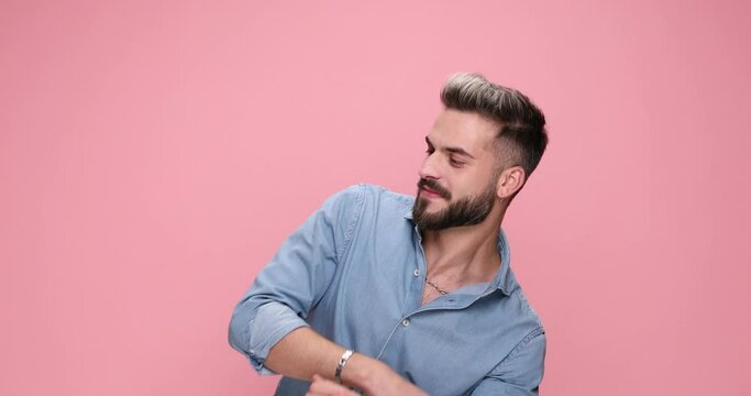 attractive casual man dancing around, pointing finger, gesturing call me, shooting with his finger gun against pink background