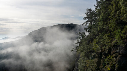 Blick in den Morgenstunden von den Affensteinen zum Kleinen Winterberg. Die Sonne schickt ihre ersten wärmenden Strahlen durch den dichten Nebel in die Bergwelt des Nationalparkes Sächsische Schweiz.