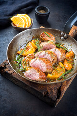 Traditional fried pork filet medaillons in with orange slices and herbs offered as close-up in a rustic wrought iron skillet - obrazy, fototapety, plakaty