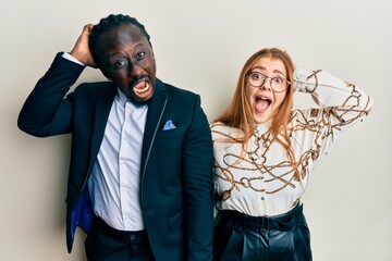 Young interracial couple wearing business and elegant clothes crazy and scared with hands on head, afraid and surprised of shock with open mouth