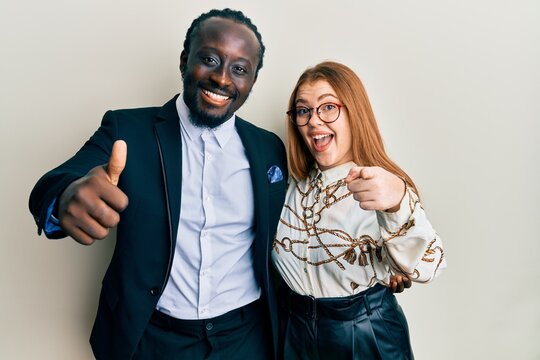 Young interracial couple wearing business and elegant clothes pointing fingers to camera with happy and funny face. good energy and vibes.