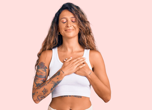 Young hispanic woman with tattoo wearing casual clothes smiling with hands on chest with closed eyes and grateful gesture on face. health concept.