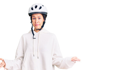 Beautiful brunette young woman wearing bike helmet and sporty clothes clueless and confused expression with arms and hands raised. doubt concept.