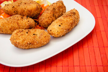 Plato con croquetas caseras y ensalada, sobre un mantel de caña roja