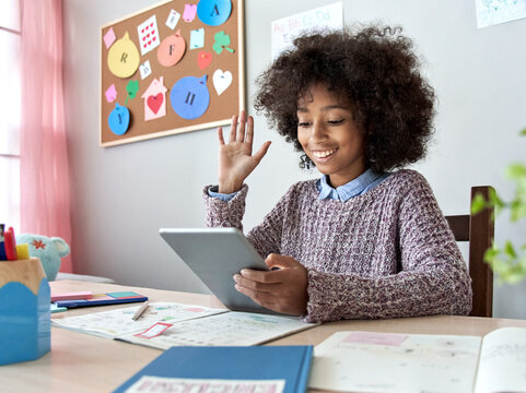 Happy african american mixed race kid girl waving hand talking with remote web teacher on social distance video conference call elearning virtual class on tablet. Children learning at home concept.