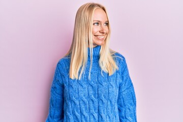 Young blonde girl wearing wool winter sweater looking away to side with smile on face, natural expression. laughing confident.