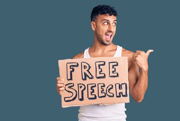 Young hispanic man holding free speech banner pointing thumb up to the side smiling happy with open mouth