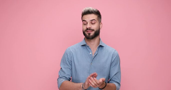 attractive young casual man applauding although he is feeling bored and yawning against pink background