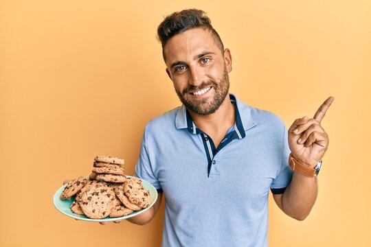 Handsome man with beard holding cookies smiling happy pointing with hand and finger to the side