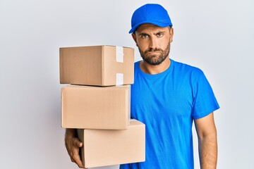 Handsome man with beard wearing courier uniform holding delivery packages skeptic and nervous, frowning upset because of problem. negative person.