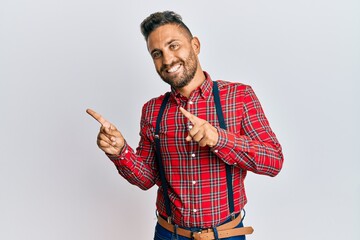 Handsome man with beard wearing hipster elegant look smiling and looking at the camera pointing with two hands and fingers to the side.