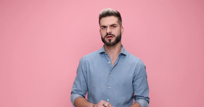 young casual man feeling angry, showing his fists, pointing his finger and sending a warning against pink background