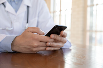 How do you feeling today. Close up of male doctor family therapist sitting at workplace making video call to patient by cellphone monitoring health state, giving recommendations, making prescriptions