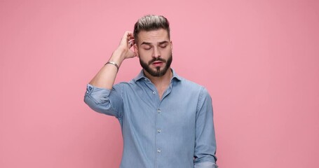 casual man scratching his head, looking around and feeling confused then pointing at the camera and smiling, celebrating on pink background