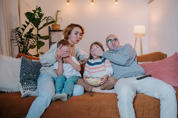 Surprised family watching television on couch, parents covering children's faces