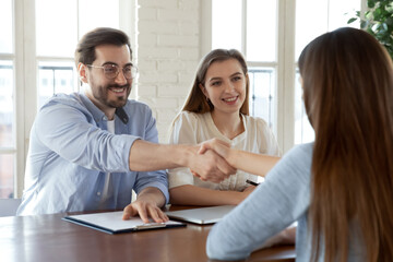 Congratulations, you are hired. Friendly man and woman employers hr colleagues greeting with handshaking young female new team member just accepted on vacancy to corporate stuff by interview results