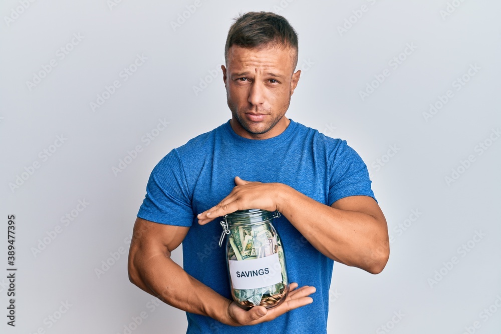 Sticker Handsome muscle man holding jar with savings skeptic and nervous, frowning upset because of problem. negative person.