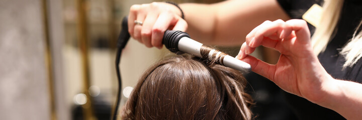 The hairdresser curls his hair with a curling iron