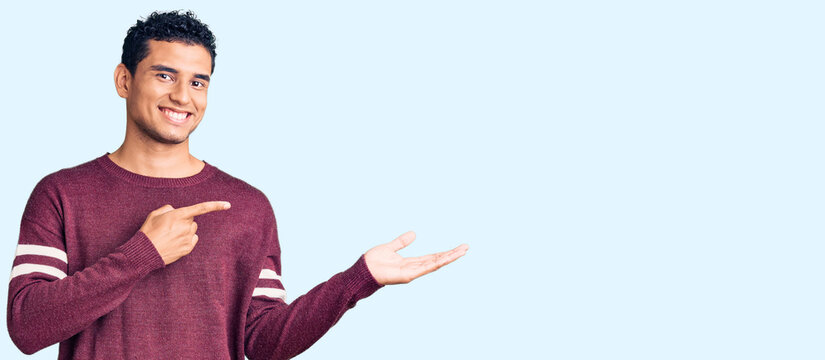 Hispanic handsome young man wearing casual clothes amazed and smiling to the camera while presenting with hand and pointing with finger.