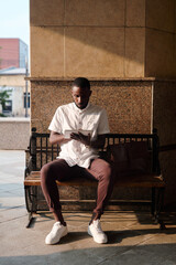 Young contemporary businessman in smart casualwear sitting on bench by wall