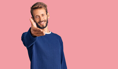 Handsome blond man with beard wearing casual sweater smiling cheerful offering palm hand giving assistance and acceptance.