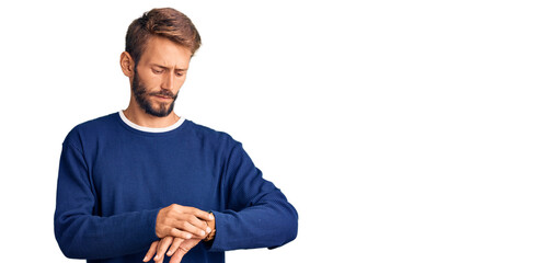 Handsome blond man with beard wearing casual sweater checking the time on wrist watch, relaxed and confident